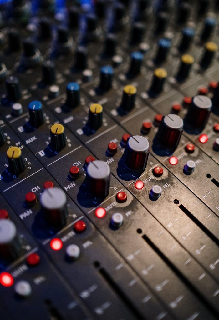 Detailed view of audio mixer controls with various knobs and lights for sound engineering.