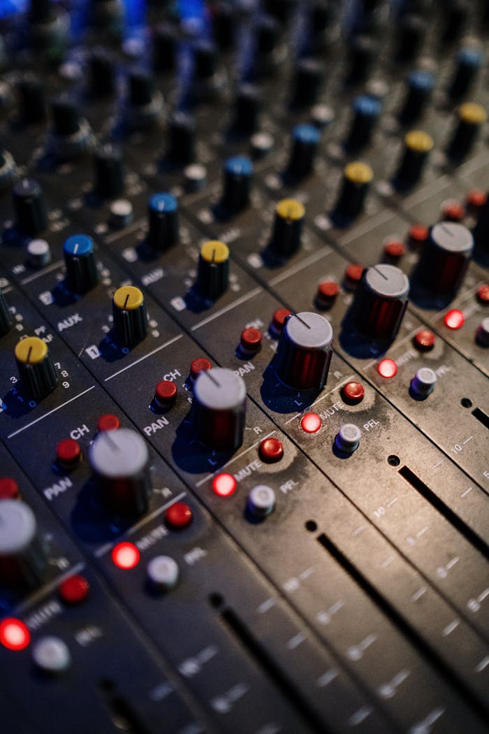Detailed view of audio mixer controls with various knobs and lights for sound engineering.